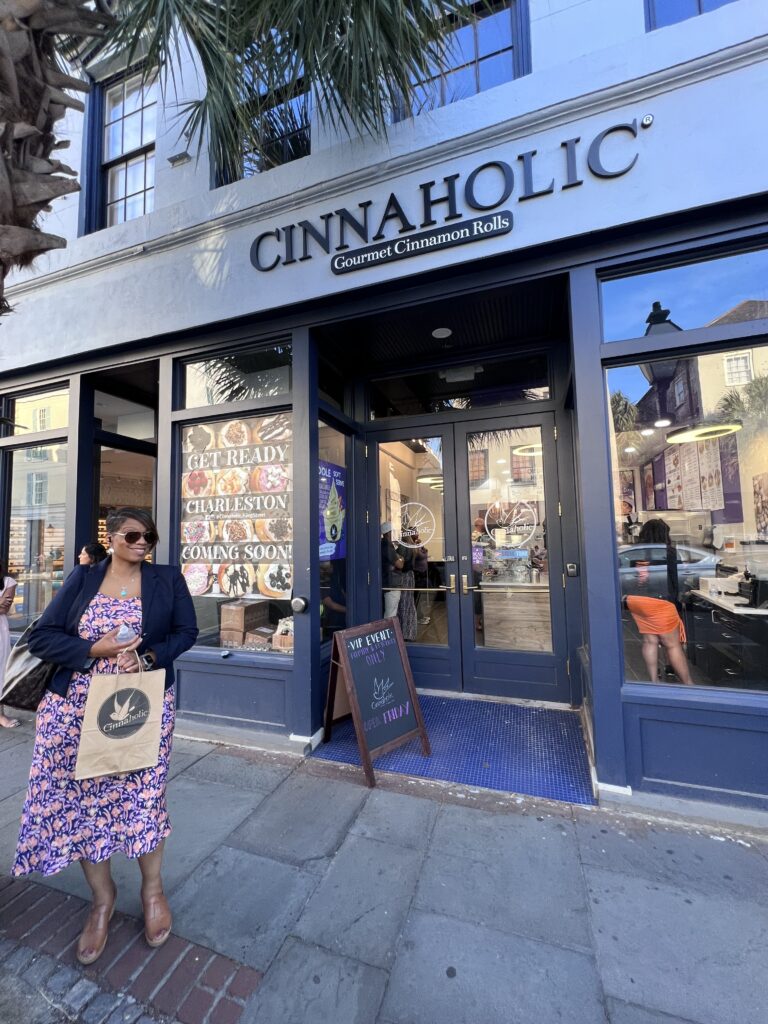 A woman standing in front of a store with a sign that says cinnaholic.