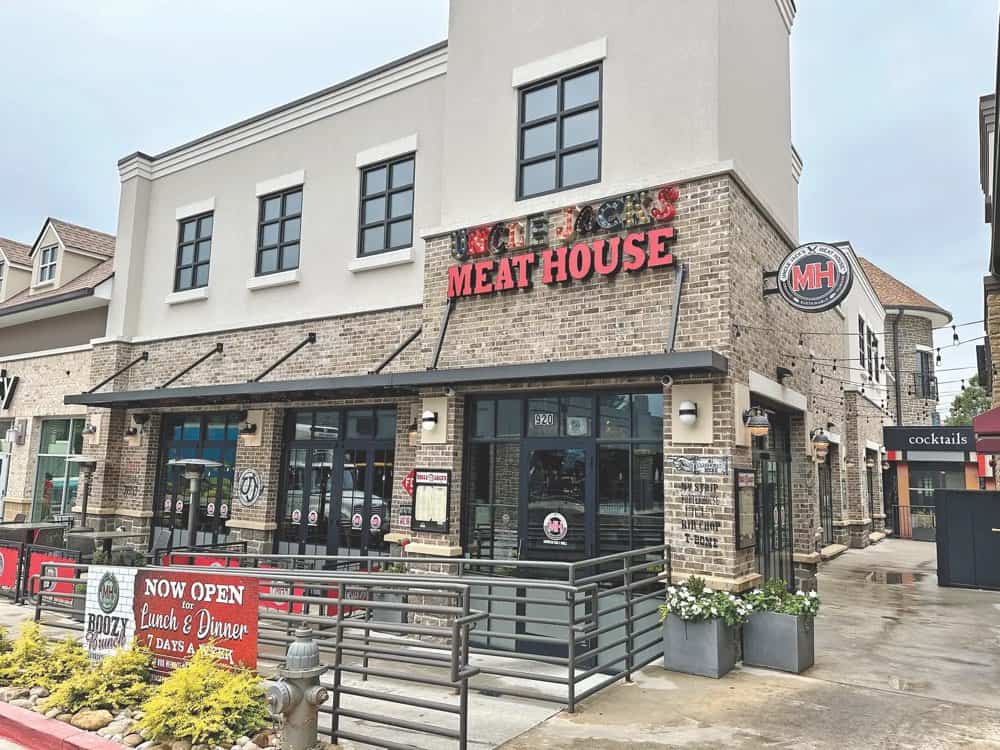 Street view of a two-story brick building with a sign reading "Meat House." The entrance is at ground level, and a banner advertises lunch and dinner. The building is adjacent to other shops.