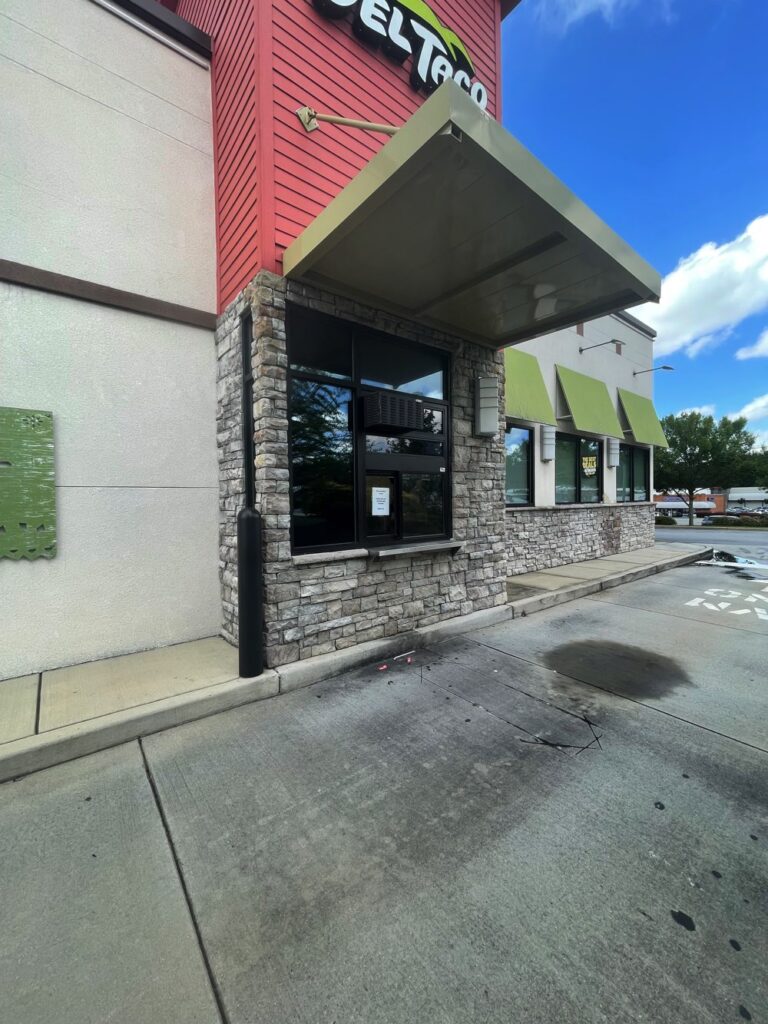 Del Taco drive-thru window with a green awning, stone exterior, and concrete pavement under a blue sky—perfect for those seeking a freestanding restaurant or drive thru for lease in Kennesaw GA.