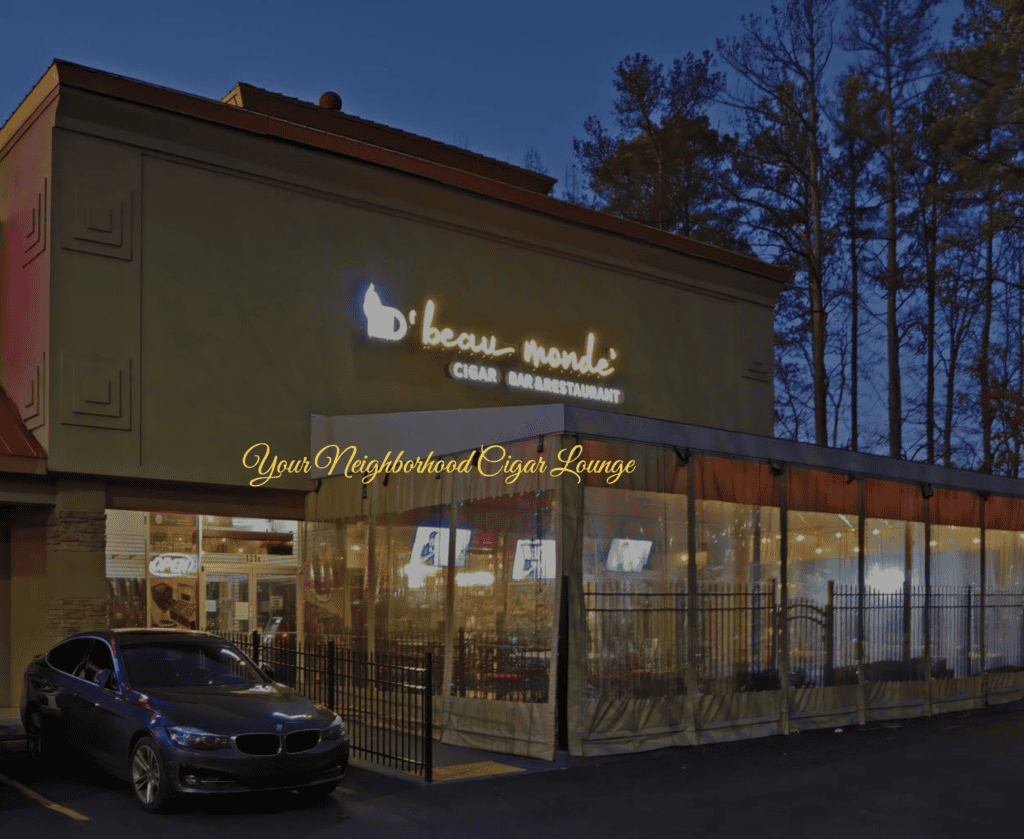 Exterior view of d'beau-monde Cigar Bar Restaurant at dusk, with a parked car in front and illuminated signage reading "Your Neighborhood Cigar Lounge.